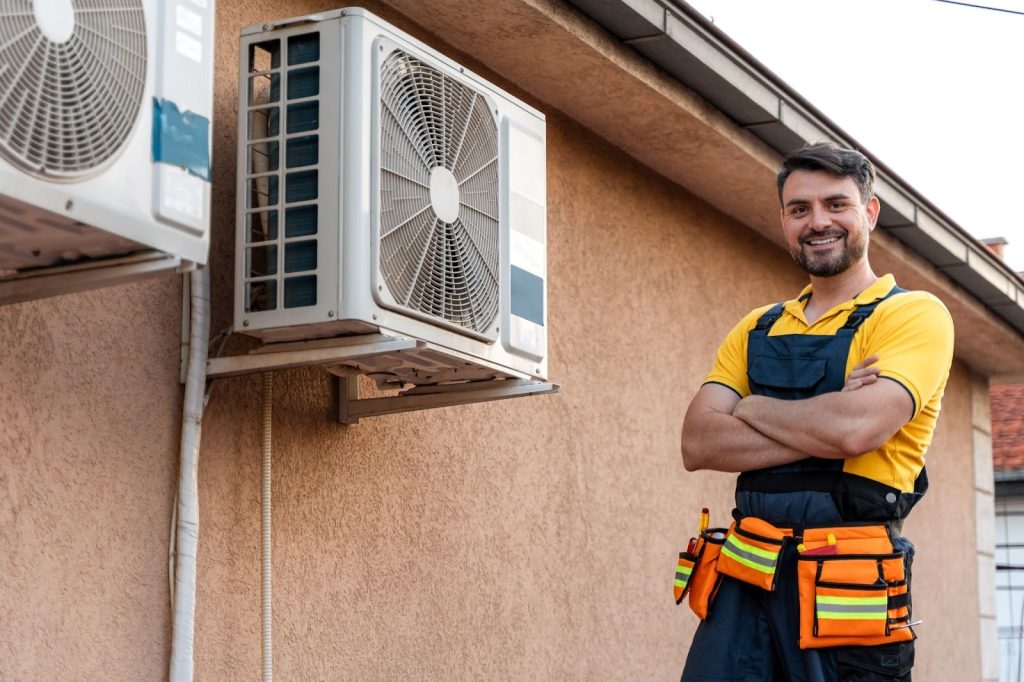 HVAC service technician proudly standing beside outdoor air conditioner condensers after repair