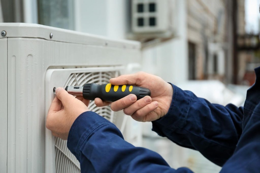 Close-up of a technician’s hand using a screwdriver to open a heat pump unit panel for inspection and maintenance